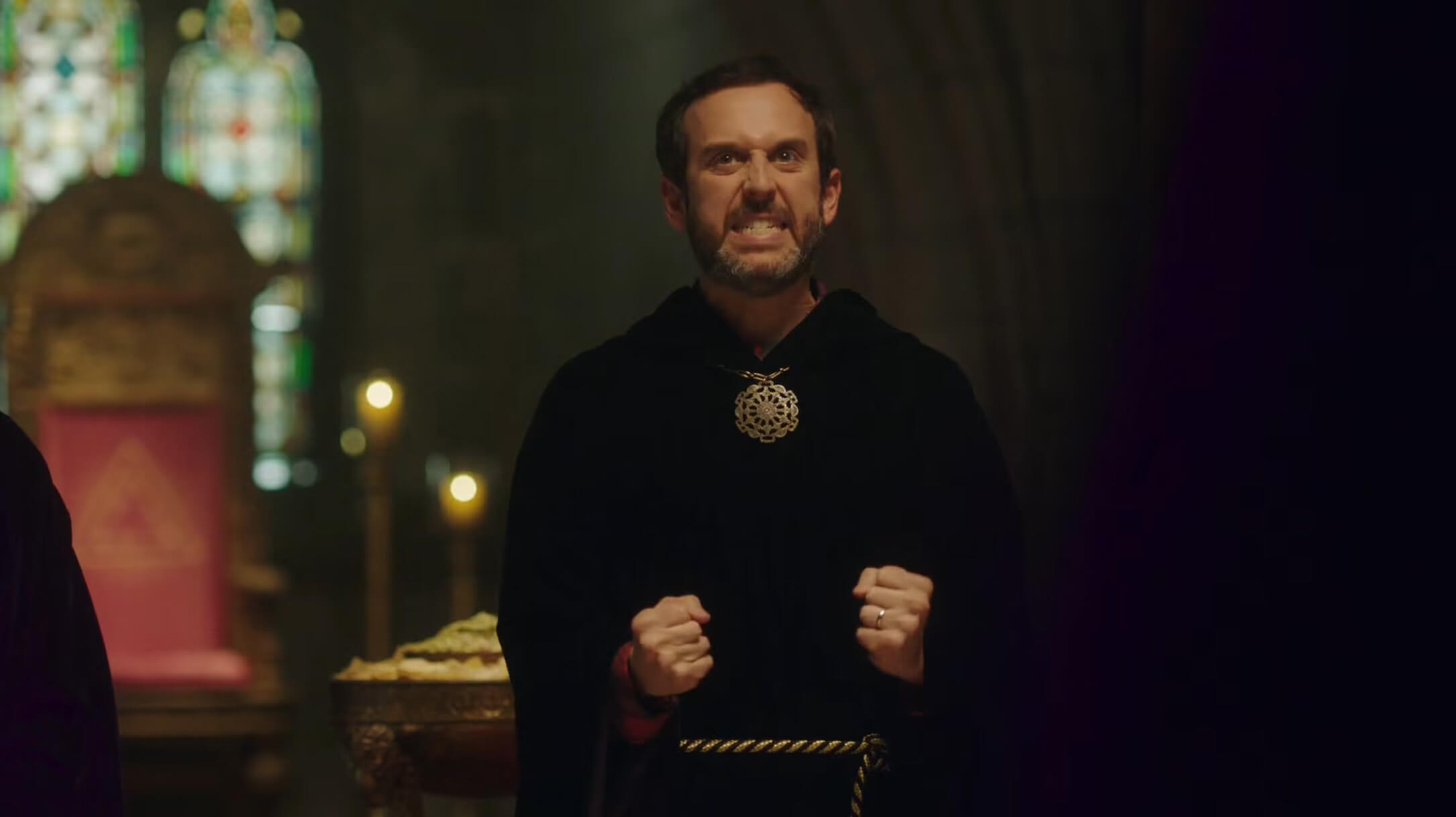 Intense looking man in black robe with closed fists and gritted teeth