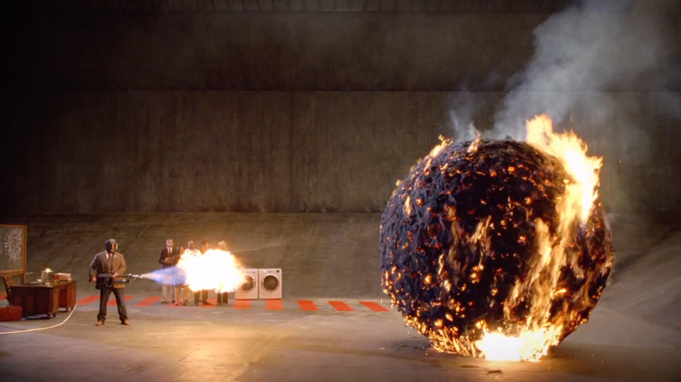 Man with blowtorch setting fire to large ball while people observe